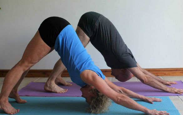 A man and woman holding the downward dog yoga position on their yoga mats.