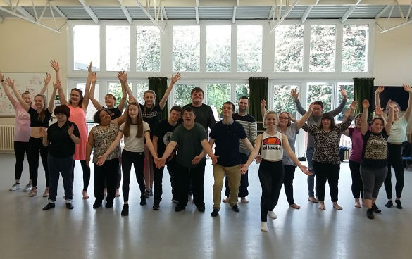 Performers in the studio all facing forwards and holding hands.