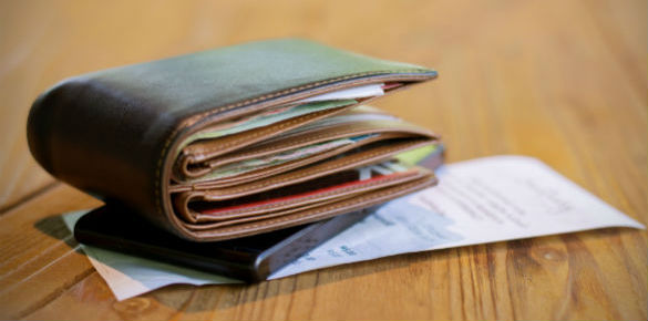 The side of a brown wallet which is sitting on top of a mobile phone and a receipt.