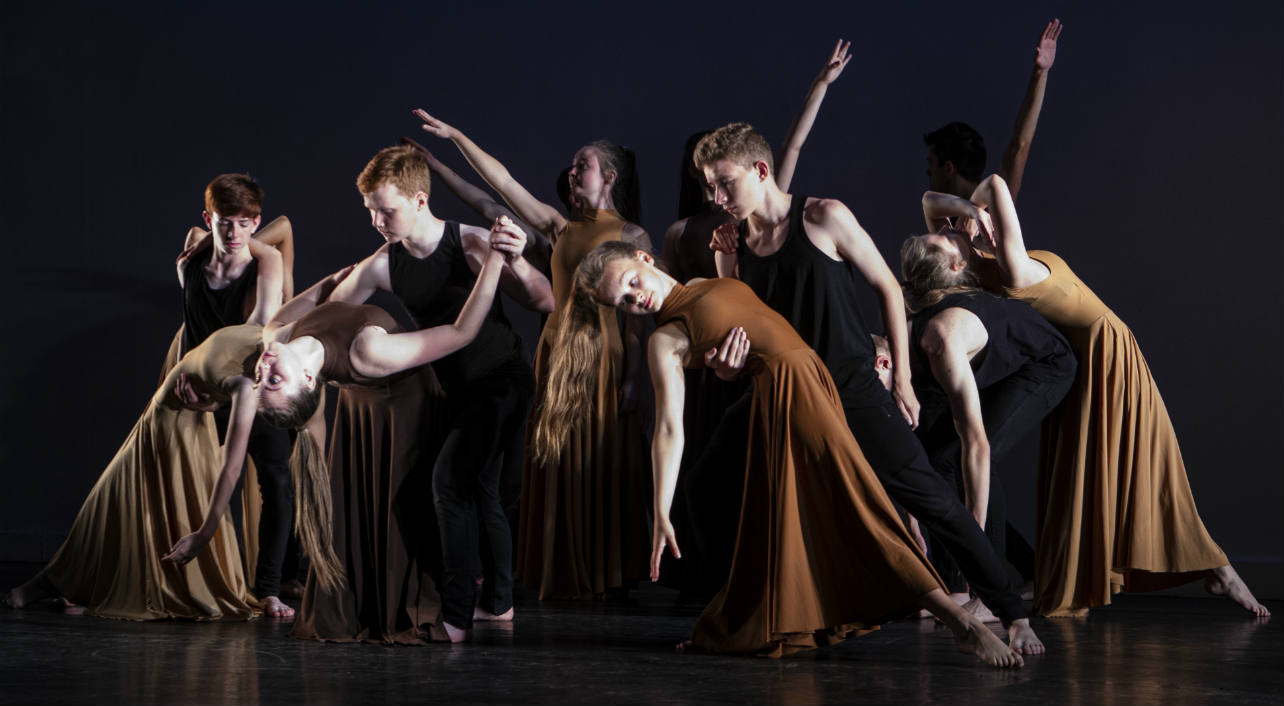 A group of teenage dancers in a studio lunging during a warm up. 