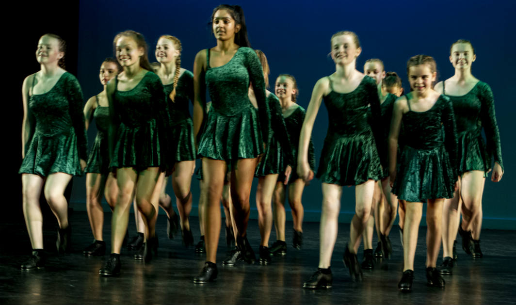 Male and female tap dancers jumping up in the air with their arms above their heads.