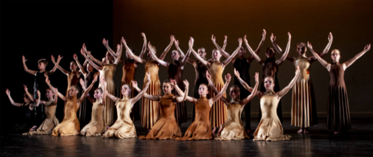 Young female dancer standing with her arms out surrounded by male dancers on one knee.