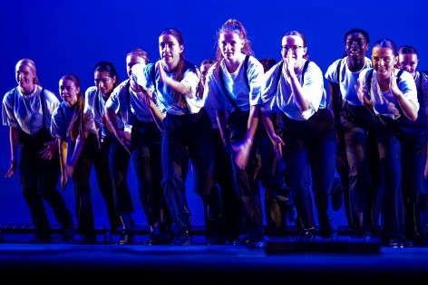 Male and female tap dancers jumping up in the air with their arms above their heads.