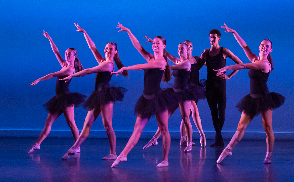 A group of young, female ballet dancers in blue leotards dancing on stage